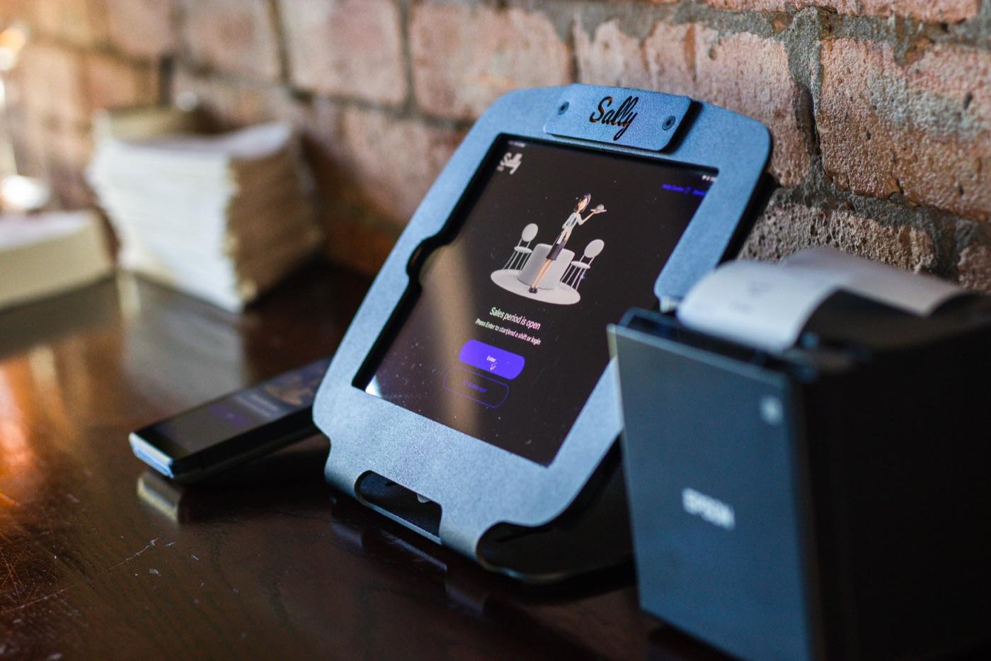 Sally POS on a tablet stand beside a receipt printer on a bar